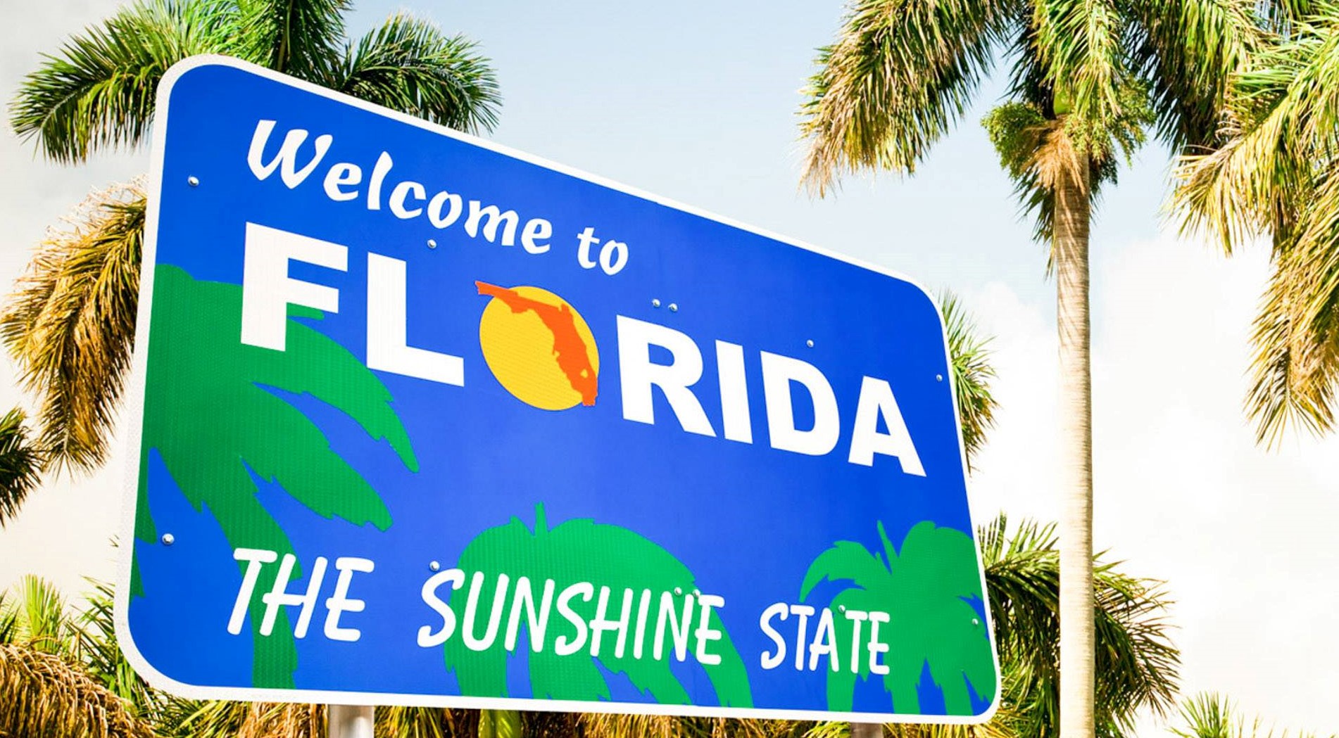 A beautiful "Welcome to Florida - The Sunshine State" sign in front of iconic palm trees