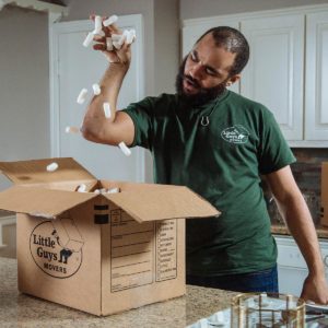 A Little Guy hilariously sprinkles packing peanuts into a moving box.